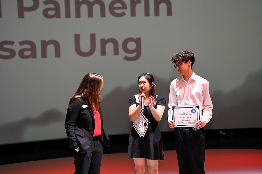 three people standing where the people on the outside are listening to the middle person speak into a microphone