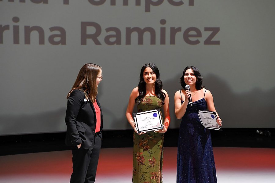 a person with their hands in their pockets standing next to two other people who are wearing dresses