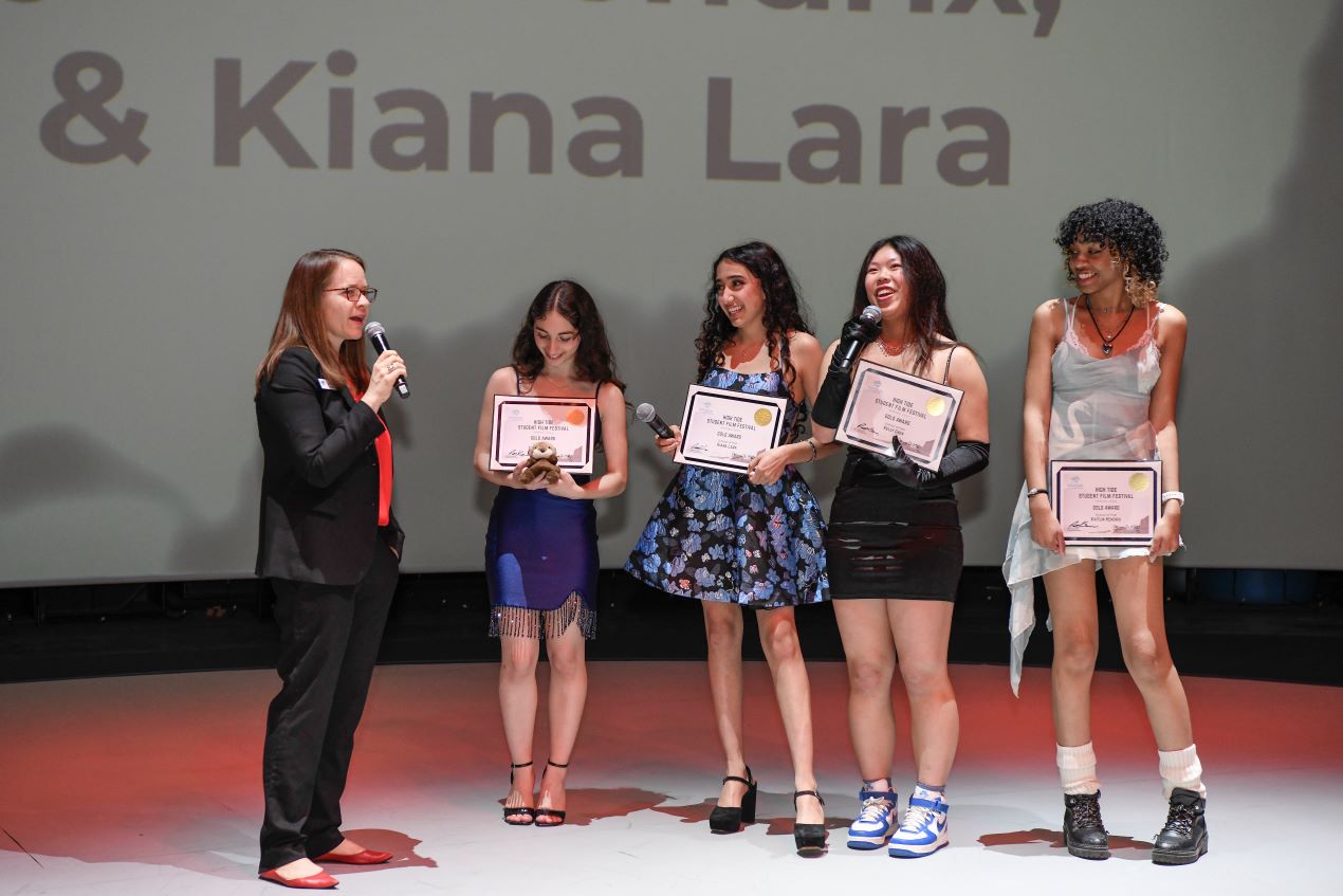 one person standing speaking into a microphone with four other people standing side by side