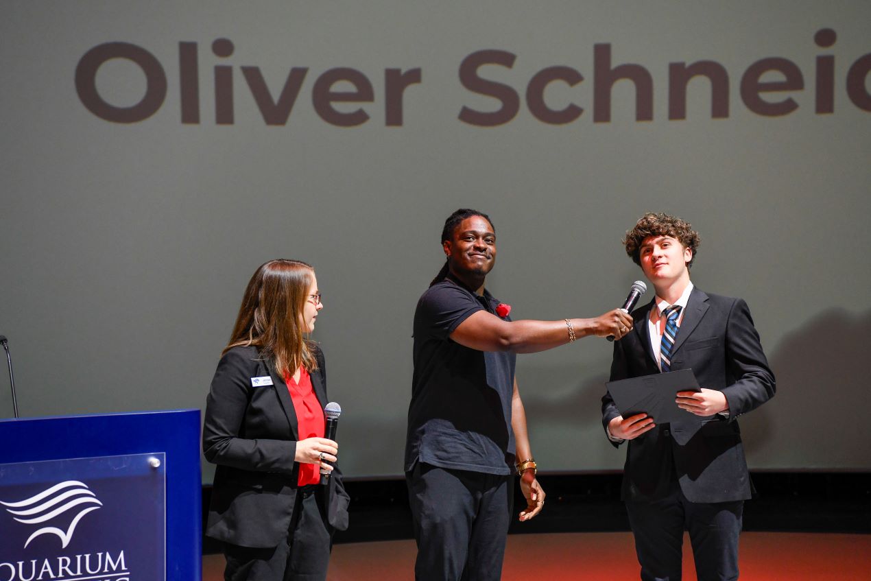 three people standing near a podium with the Aquarium logo